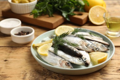 Photo of Fresh raw sprats, lemon and dill on wooden table, closeup