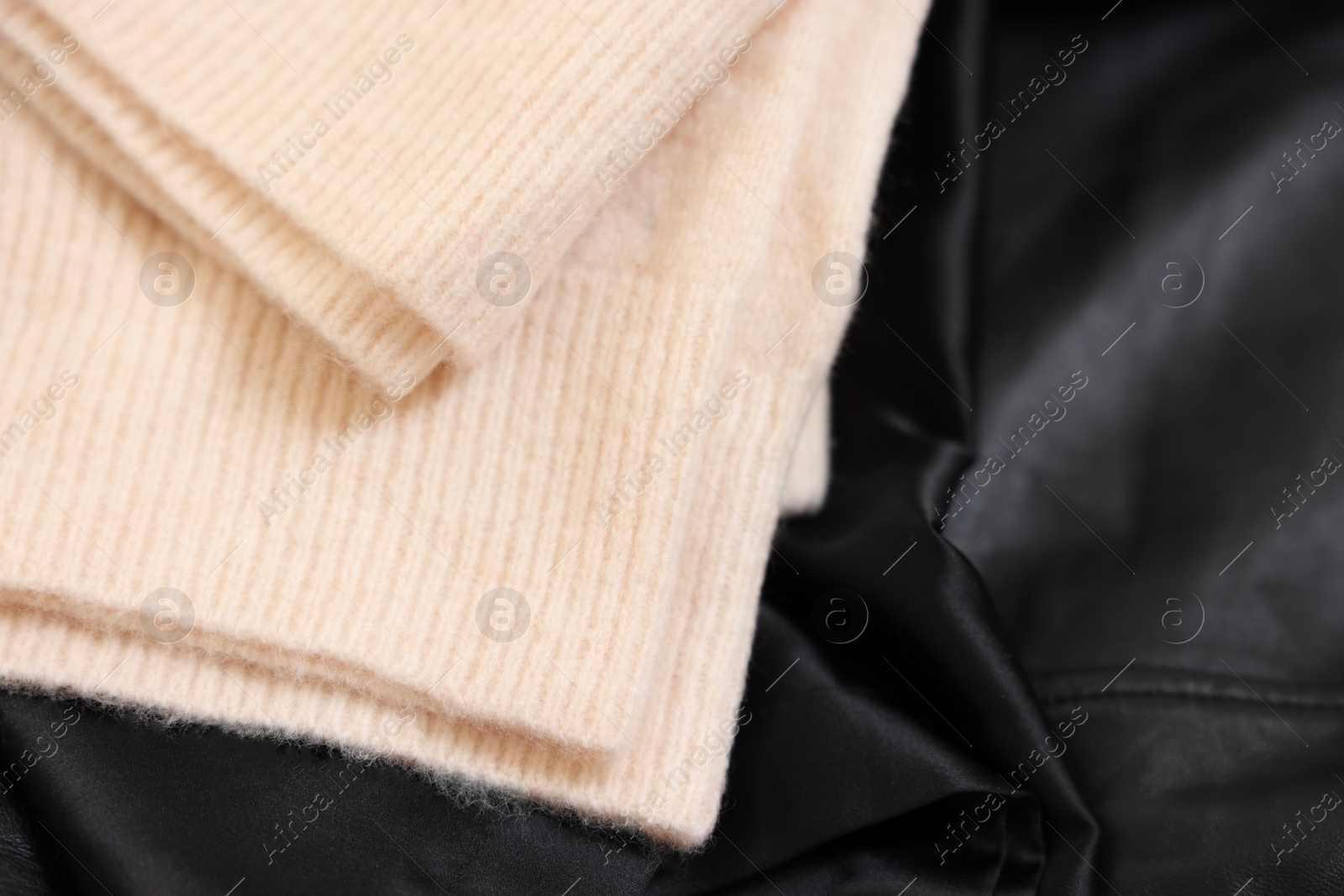 Photo of Soft beige sweater on black fabric, top view