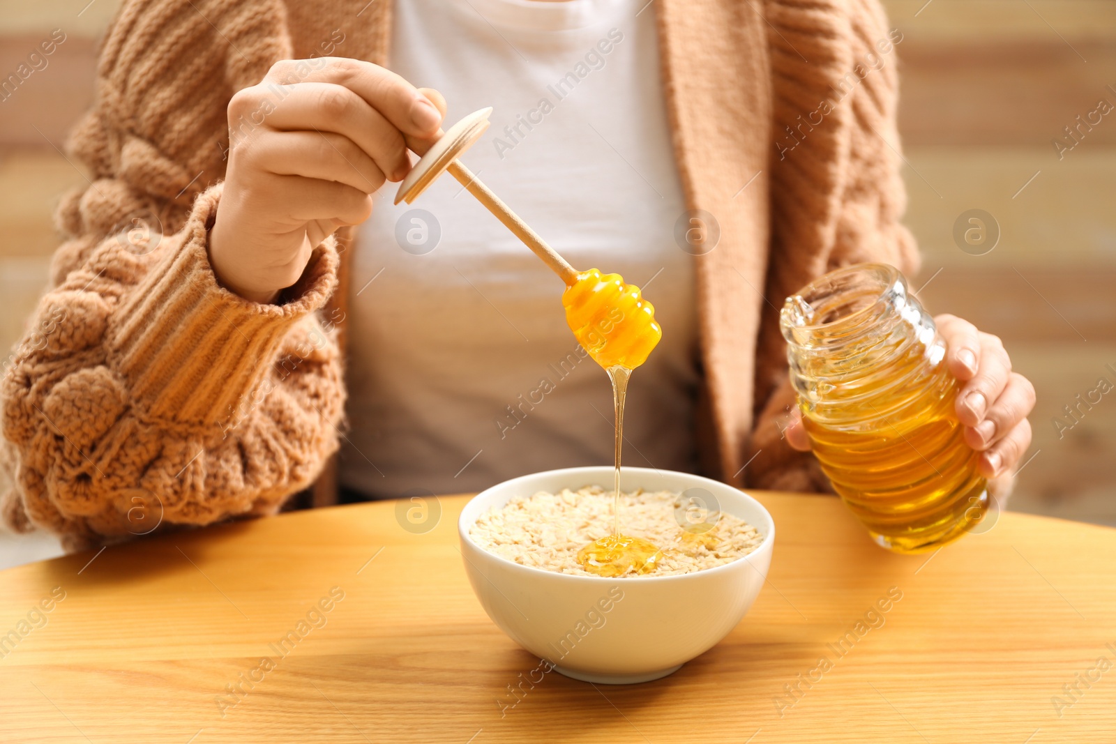 Photo of Woman adding honey to oatmeal at wooden table, closeup