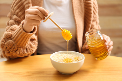 Woman adding honey to oatmeal at wooden table, closeup