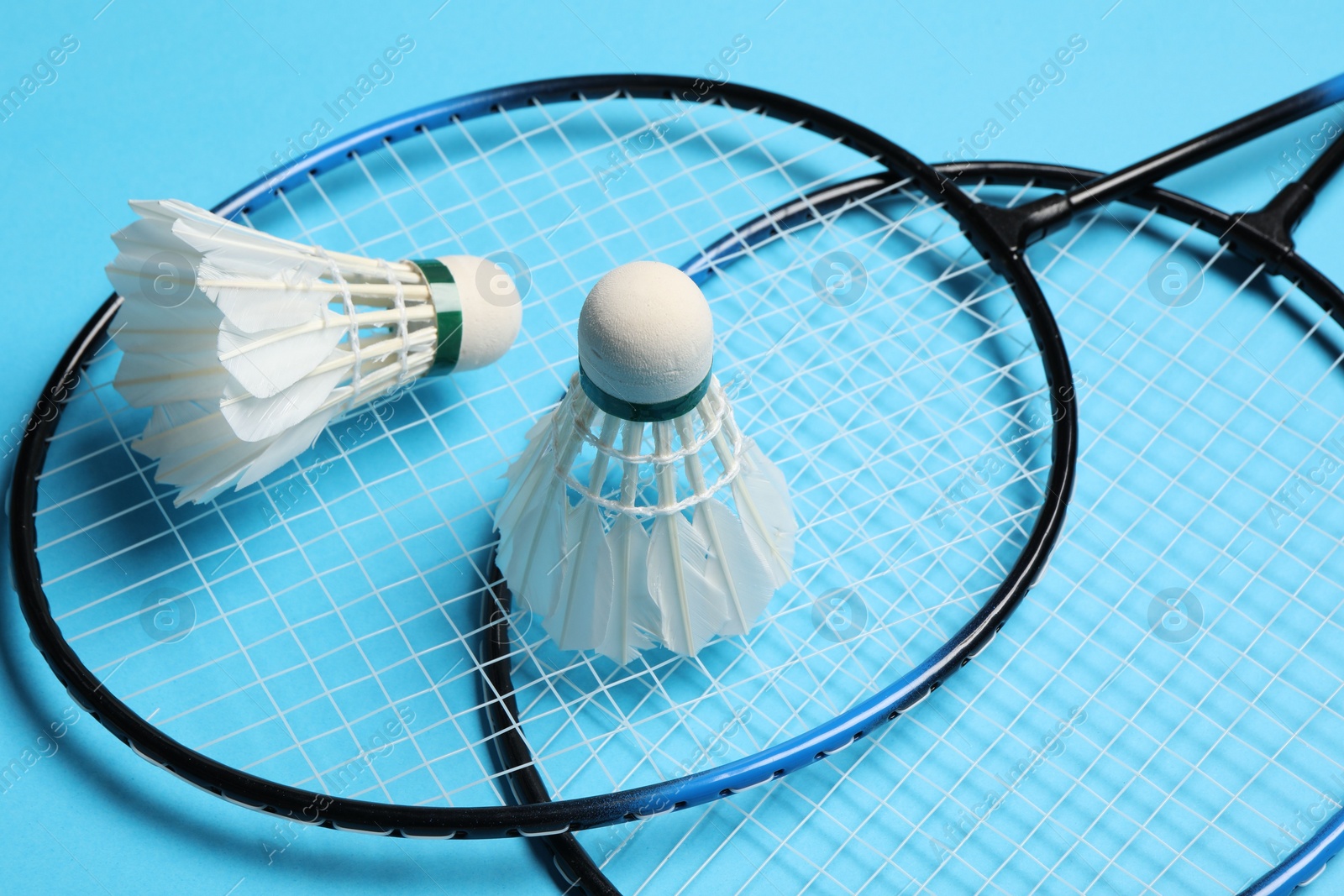 Photo of Feather badminton shuttlecocks and rackets on light blue background, closeup