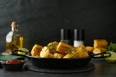 Photo of Pan with tasty grilled corn on dark grey table