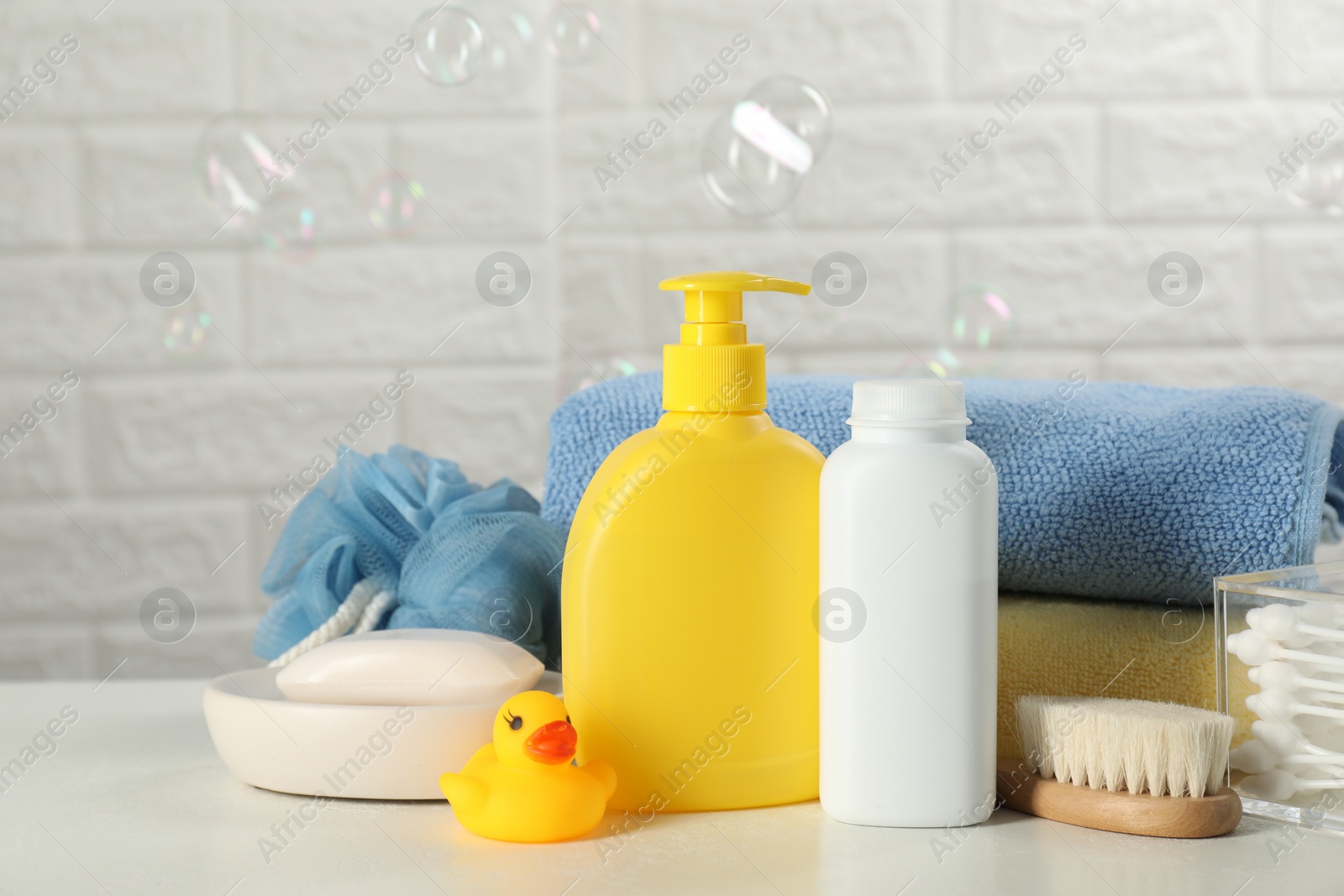 Photo of Different baby bath accessories and cosmetic products on white table against brick wall