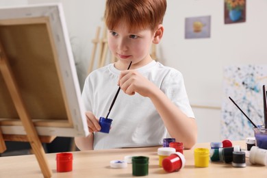 Little boy painting at table in studio. Using easel to hold canvas