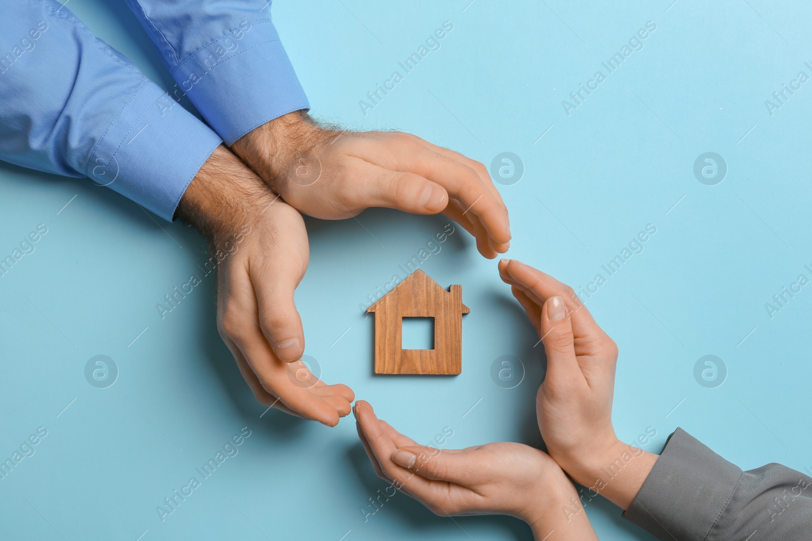 Photo of Couple holding hands near figure of house on color background, top view. Home insurance