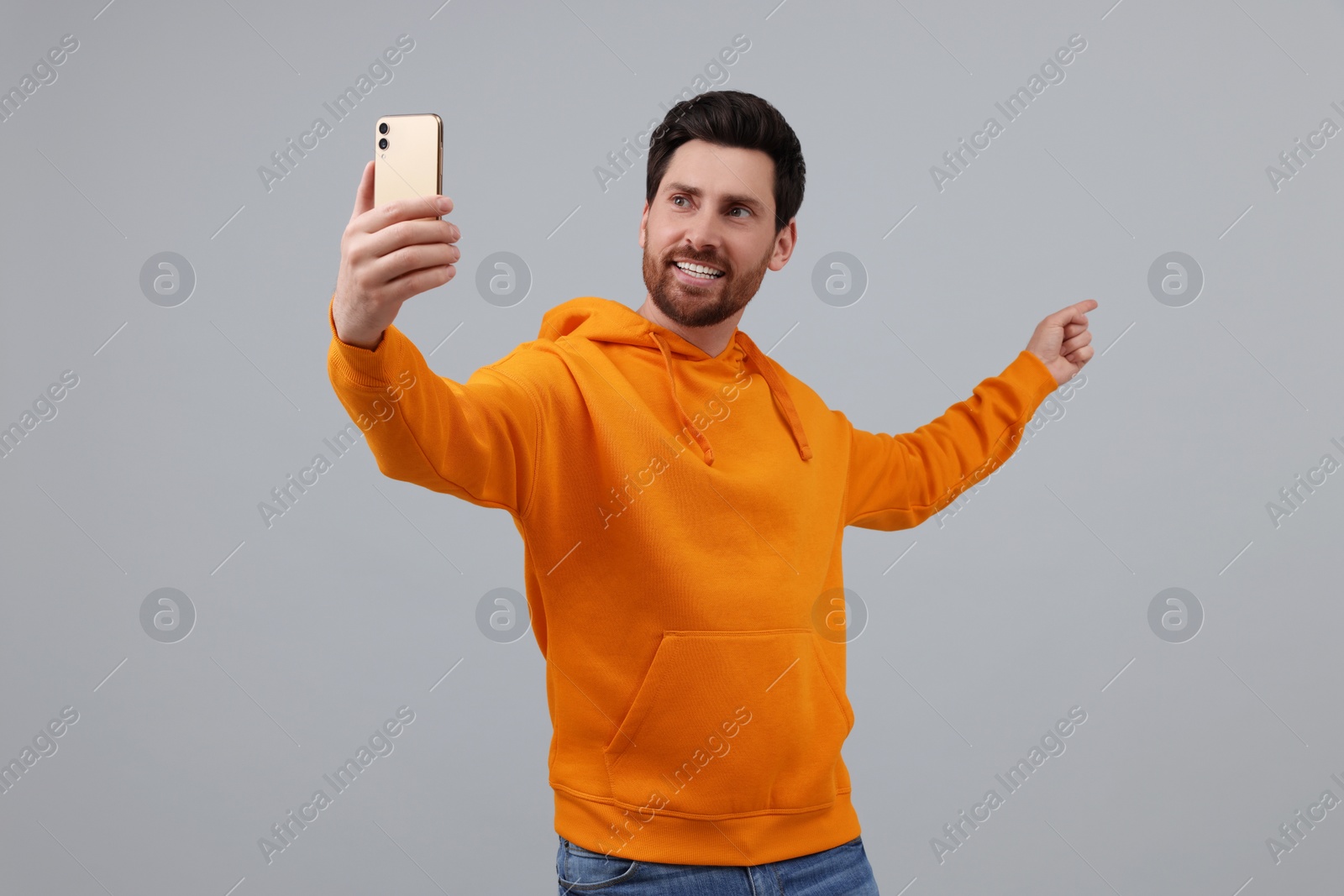 Photo of Smiling man taking selfie with smartphone on grey background