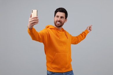 Smiling man taking selfie with smartphone on grey background