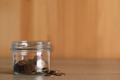 Photo of Glass jar with coins on wooden table, closeup. Space for text