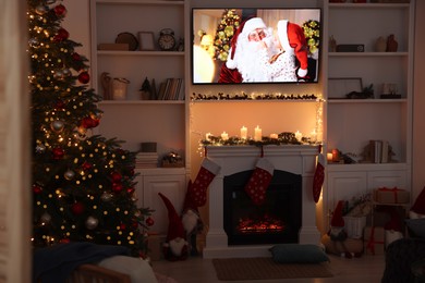 Photo of TV set with Christmas movie above fireplace in cosy room. Winter holidays atmosphere