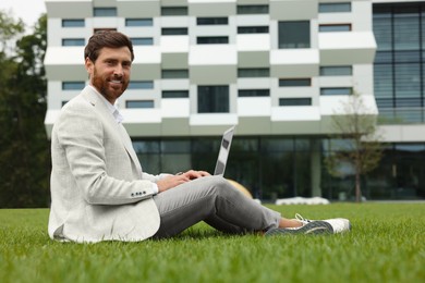 Handsome businessman with laptop on green grass outdoors