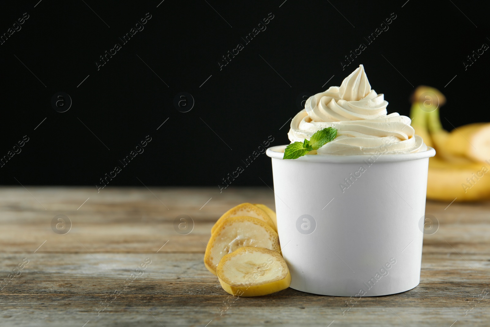 Photo of Cup with tasty frozen yogurt and banana on wooden table. Space for text