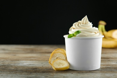 Cup with tasty frozen yogurt and banana on wooden table. Space for text