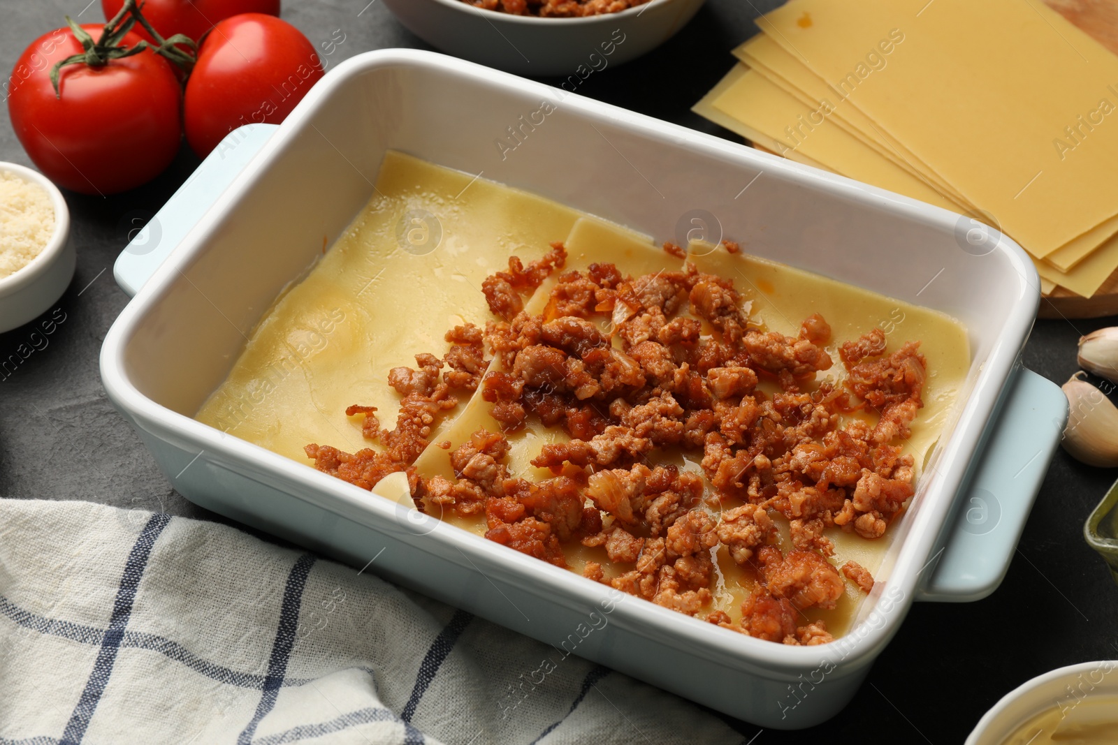 Photo of Cooking lasagna. Pasta sheets, minced meat in baking tray and tomato on table, closeup