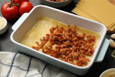 Cooking lasagna. Pasta sheets, minced meat in baking tray and tomato on table, closeup