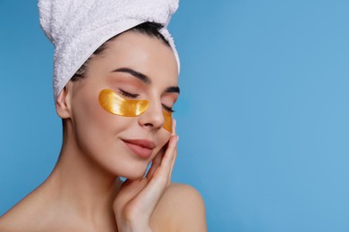 Photo of Beautiful young woman with under eye patches and hair wrapped in towel on light blue background, space for text