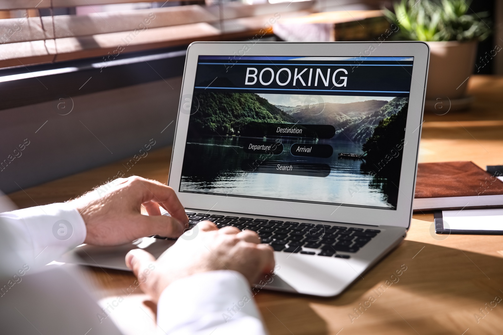 Photo of Man with laptop booking tickets online at wooden table, closeup. Travel agency concept
