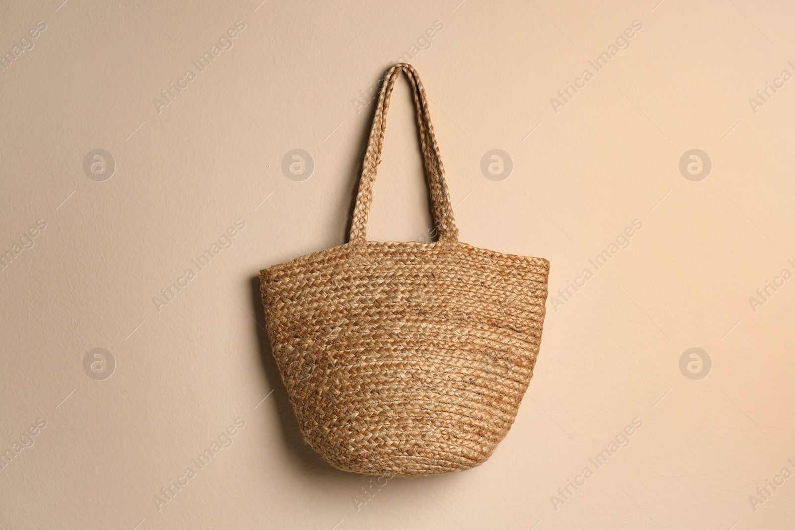 Photo of Elegant woman's straw bag hanging on beige background