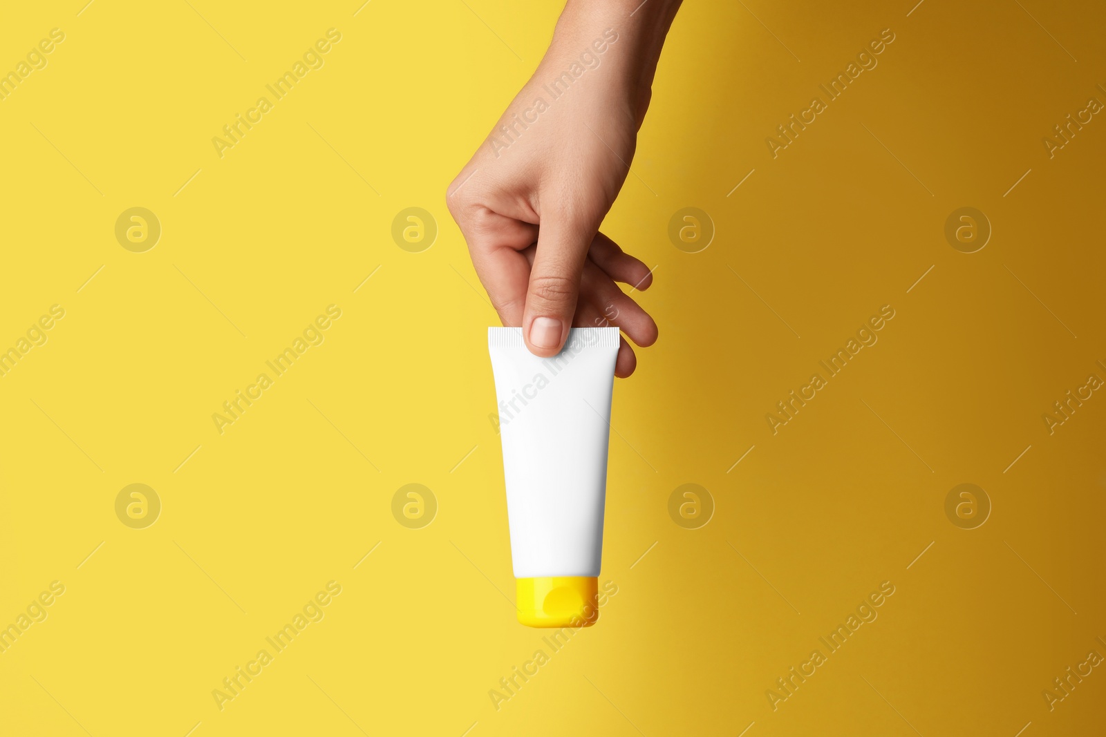 Photo of Woman holding tube of face cream on yellow background, closeup