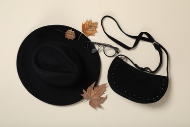 Photo of Stylish hat, bag and autumn leaves on beige background, flat lay