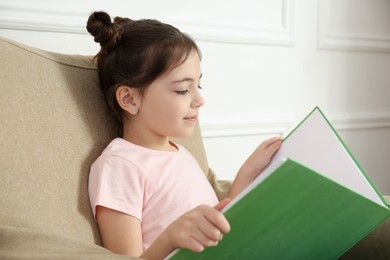 Little girl reading book in armchair at home