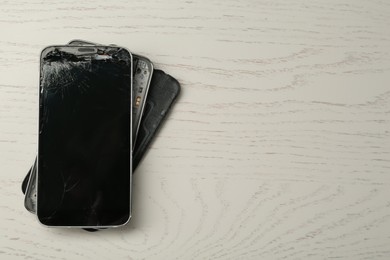 Photo of Damaged smartphone on white wooden table, top view with space for text. Device repairing