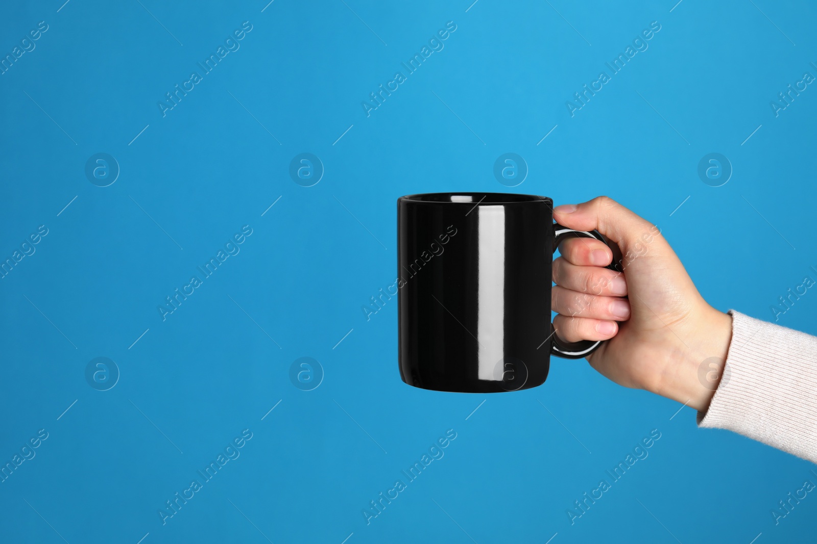 Photo of Woman holding black mug on light blue background, closeup. Space for text