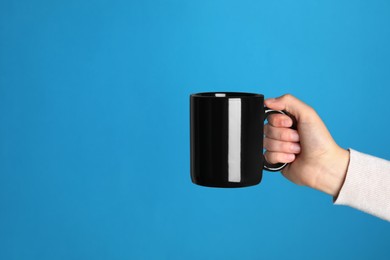 Woman holding black mug on light blue background, closeup. Space for text