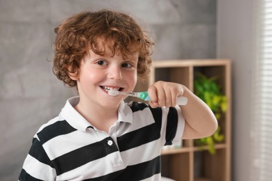 Photo of Cute little boy brushing his teeth with electric toothbrush in bathroom