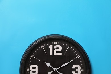 Photo of Stylish analog clock hanging on light blue wall, space for text