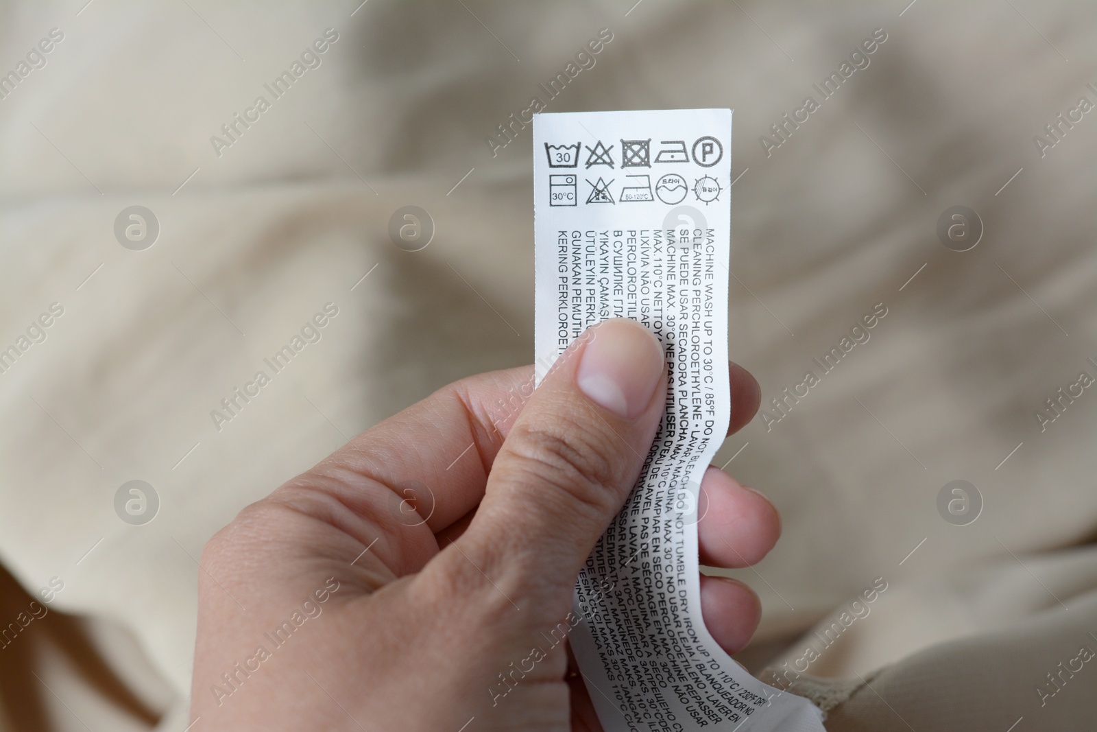 Photo of Woman holding white clothing label on beige garment, closeup