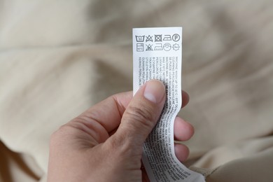 Woman holding white clothing label on beige garment, closeup