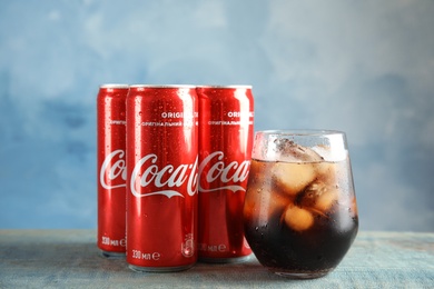 MYKOLAIV, UKRAINE - NOVEMBER 15, 2018: Glass and cans with Coca Cola on table against color background