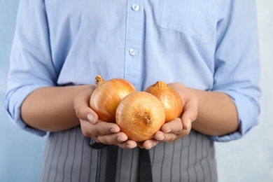 Photo of Young woman holding handful of ripe onions on blue background, closeup