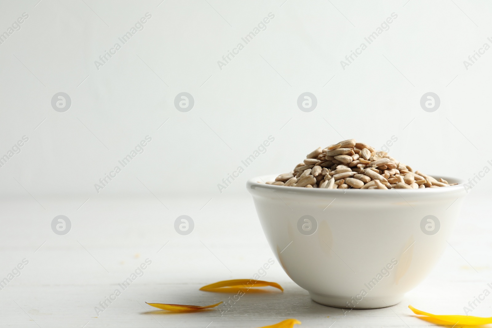 Photo of Organic sunflower seeds on white wooden table. Space for text