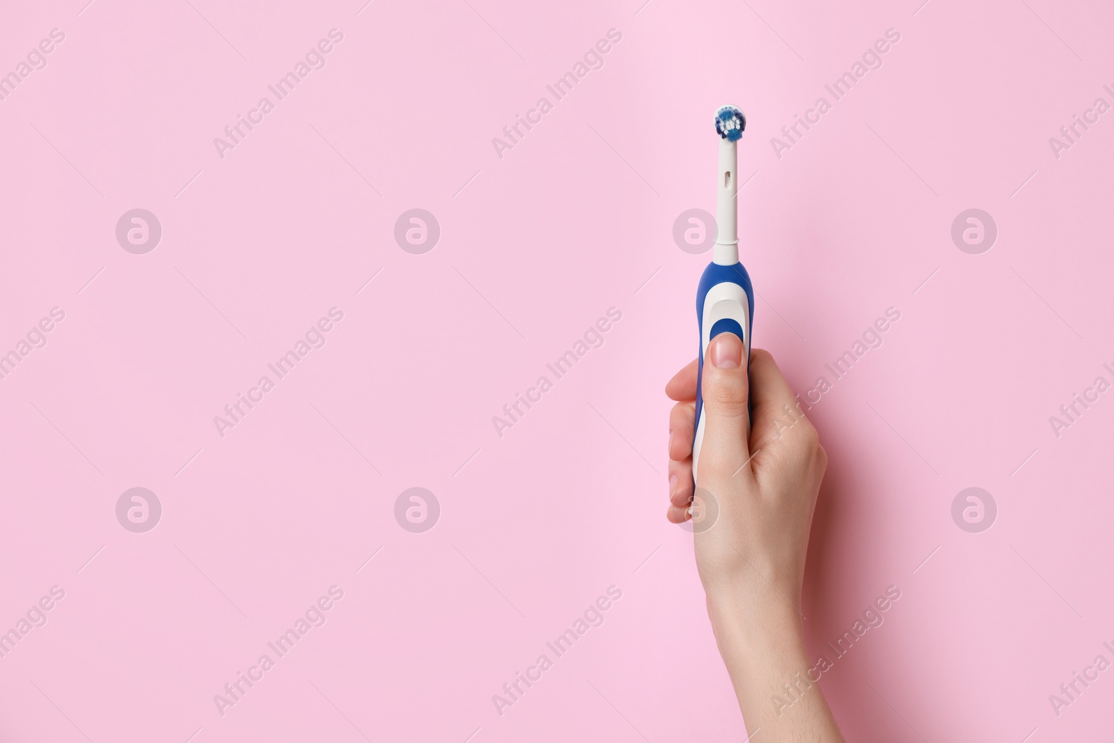 Photo of Woman holding electric toothbrush on pink background, closeup. Space for text