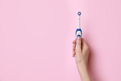 Photo of Woman holding electric toothbrush on pink background, closeup. Space for text