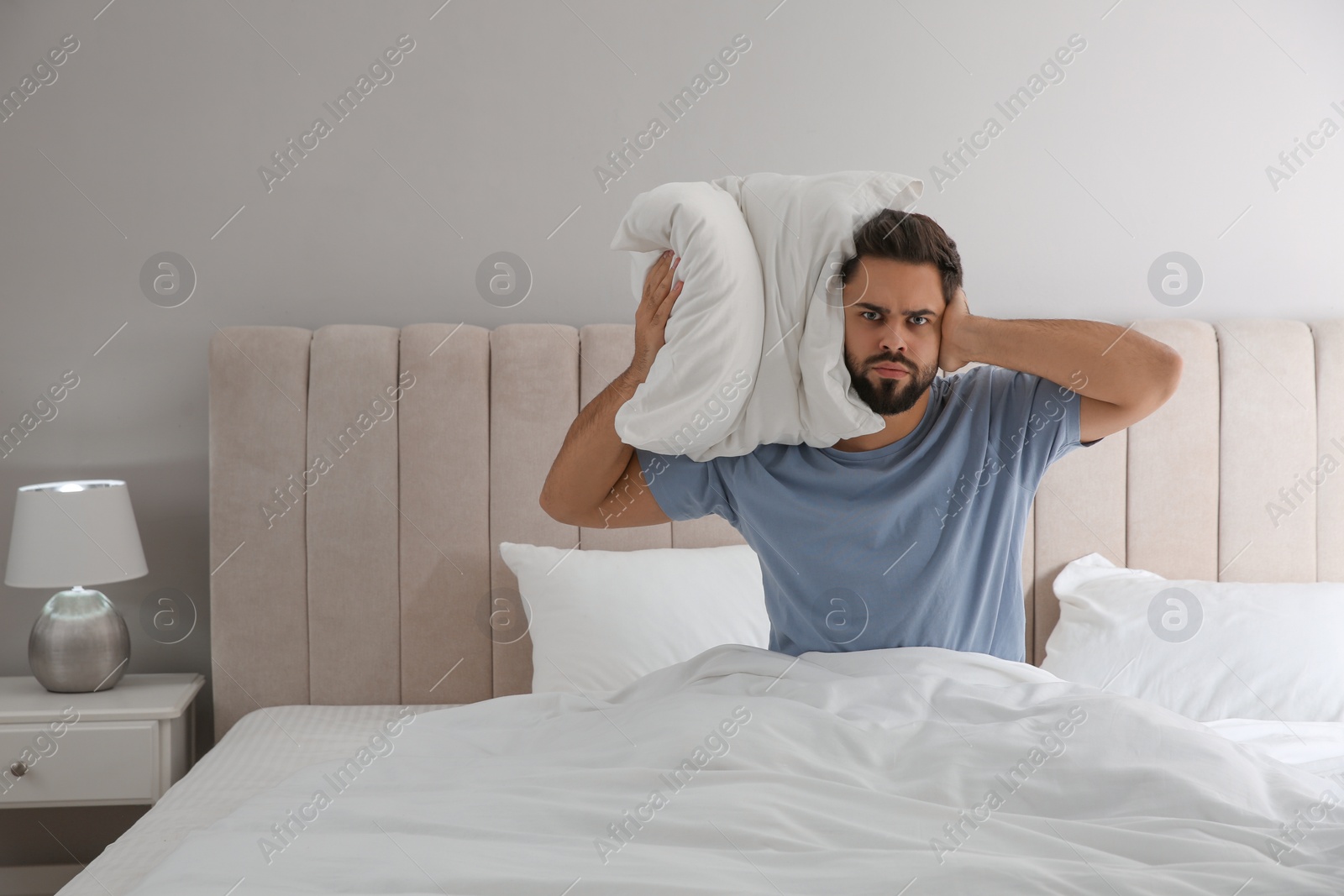 Photo of Unhappy young man covering ears in bed at home. Noisy neighbours