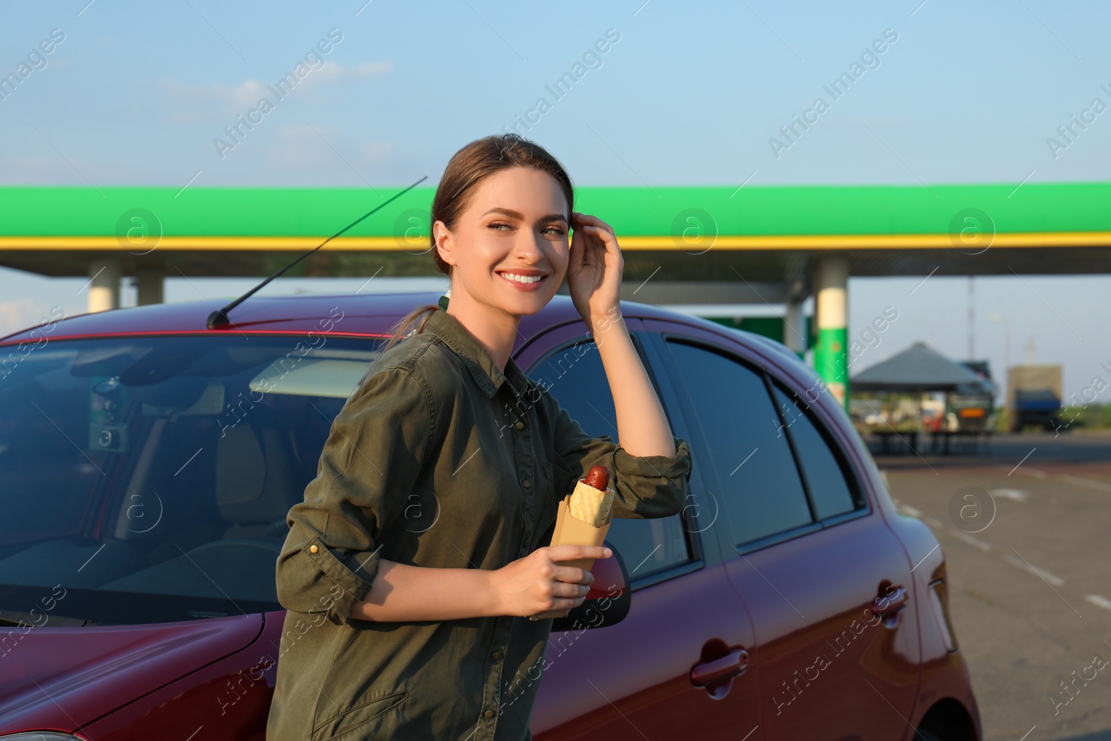 Photo of Beautiful young woman with hot dog near car at gas station