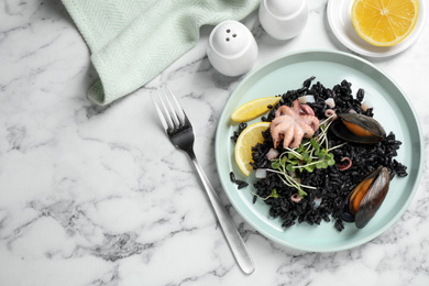 Delicious black risotto with seafood served on white marble table, flat lay