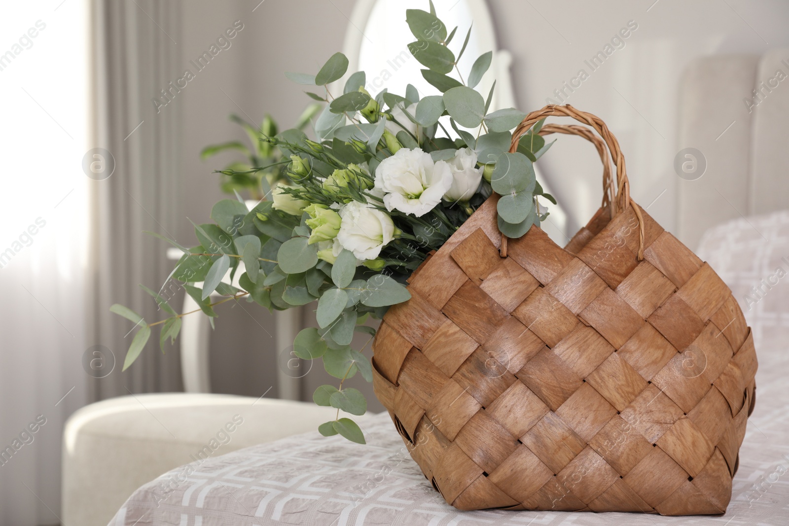 Photo of Stylish wicker basket with bouquet on bed indoors