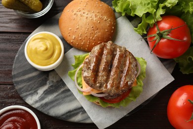 Photo of Tasty hamburger with patties, cheese and vegetables served on wooden table, flat lay