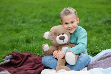 Photo of Little girl with teddy bear on plaid outdoors. Space for text