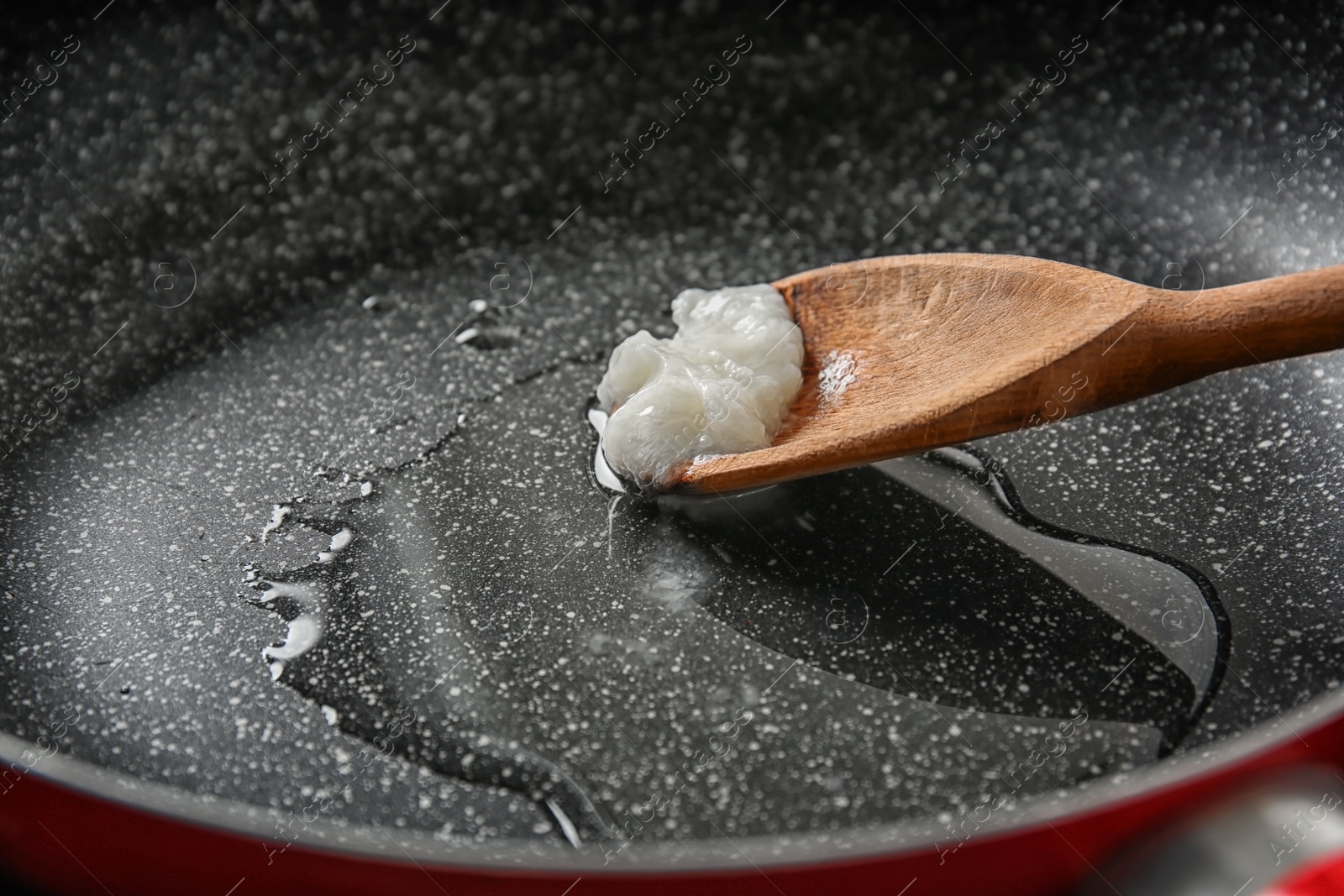 Photo of Wooden spoon with coconut oil in frying pan, closeup. Healthy cooking