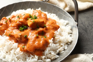 Photo of Delicious butter chicken with rice in dish and napkin on table