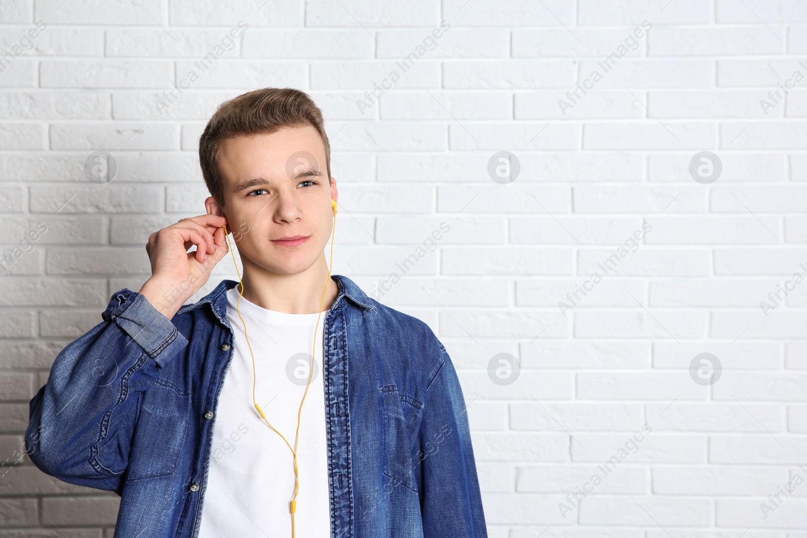 Photo of Teen boy listening to music with headphones near brick wall, space for text