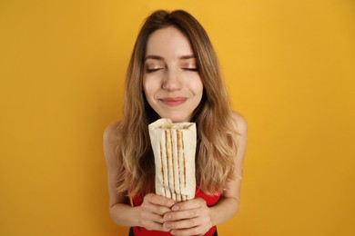 Young woman with delicious shawarma on yellow background