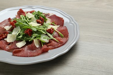 Photo of Plate of tasty bresaola salad with sun-dried tomatoes and parmesan cheese on wooden table, closeup. Space for text