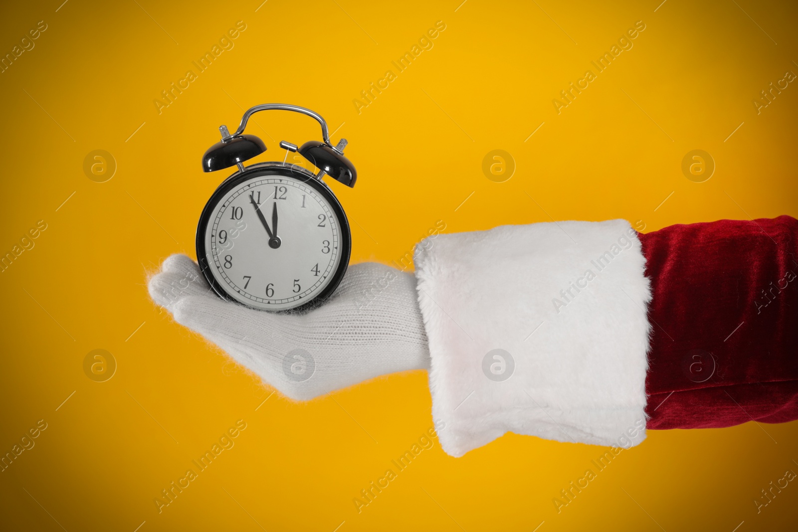 Photo of Santa Claus holding alarm clock on yellow background, closeup. Christmas countdown