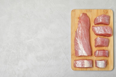 Wooden board with fresh raw meat and space for text on gray background, top view