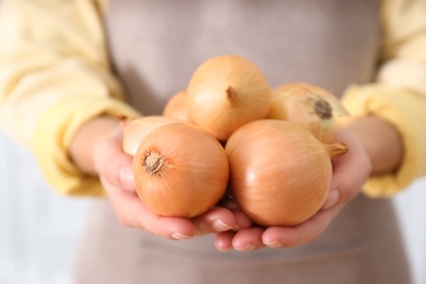 Photo of Woman holding golden onions on blurred background, closeup